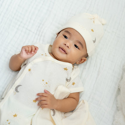 A baby wearing a kimono romper in cream by Le Petit Society, featuring a print of moon and stars.
