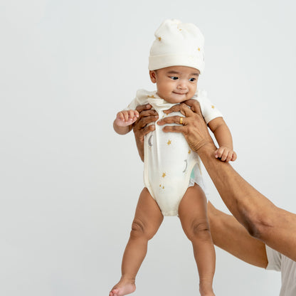 A baby wearing a kimono romper by Le Petit Society, featuring a print of moon and stars over a cream base. 
