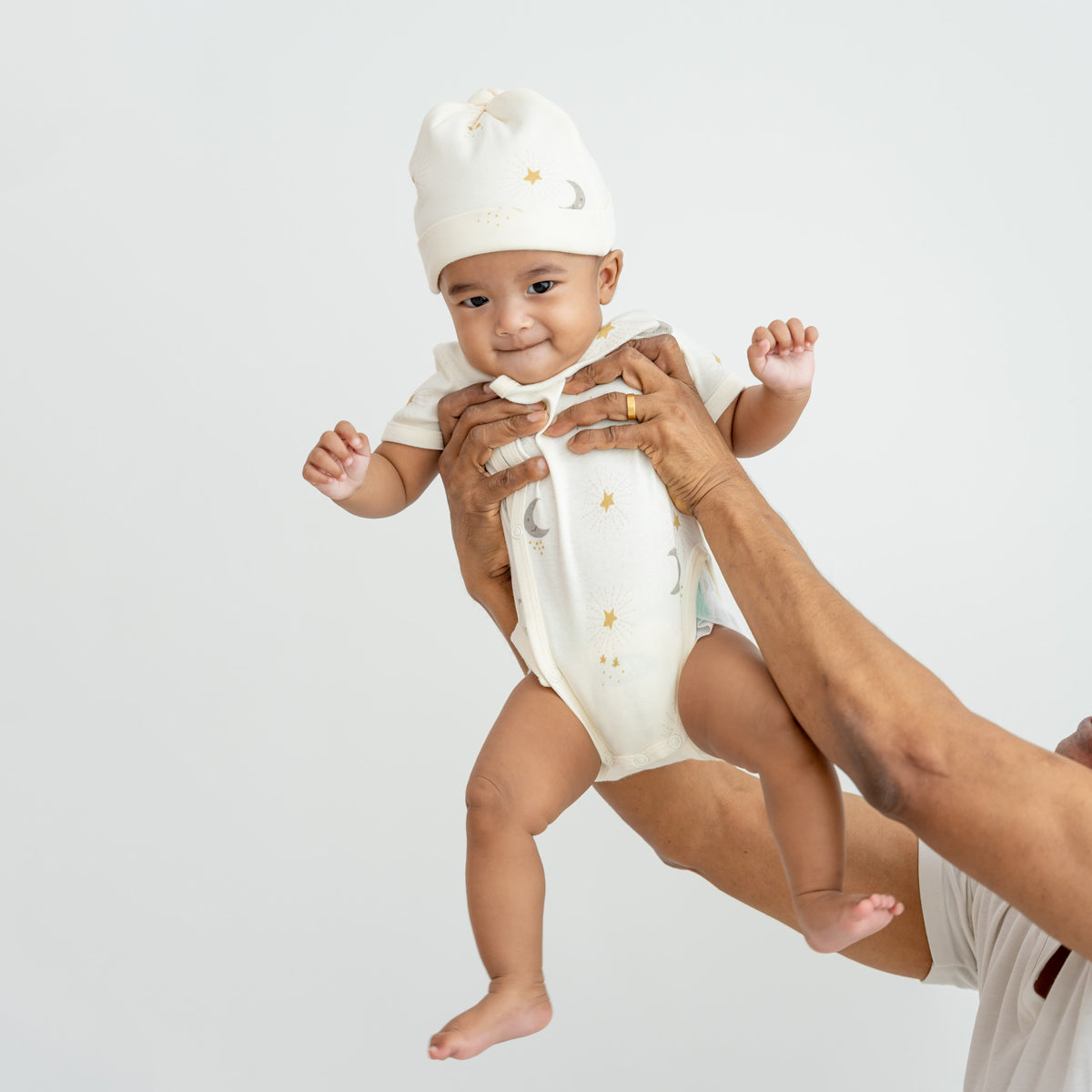 A baby wearing a kimono romper by Le Petit Society, featuring a print of moon and stars over a cream base. 
