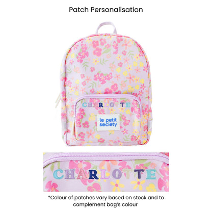 A purple preschool bag with a pink and yellow floral print and personalised name patches.