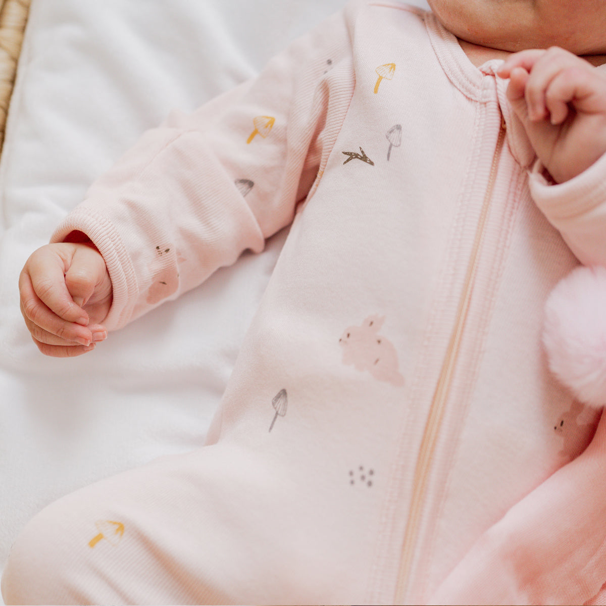 A newborn baby in an organic sleepsuit in a pink rabbit print by Le Petit Society.