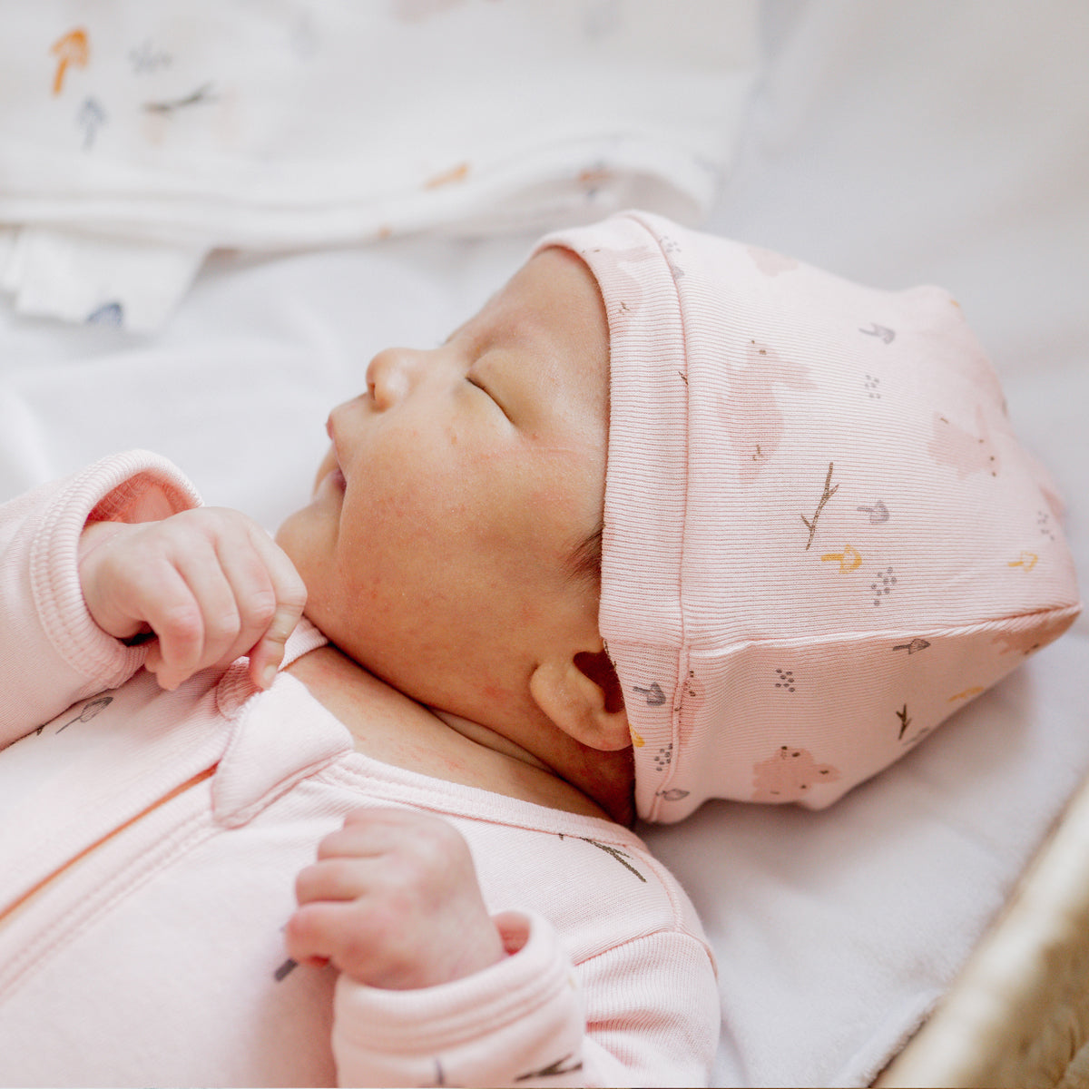 A newborn baby sleeping in an organic sleepsuit in a pink rabbit print by Le Petit Society.