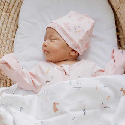 A newborn baby sleeping in an organic zip sleepsuit in a pink rabbit print by Le Petit Society.