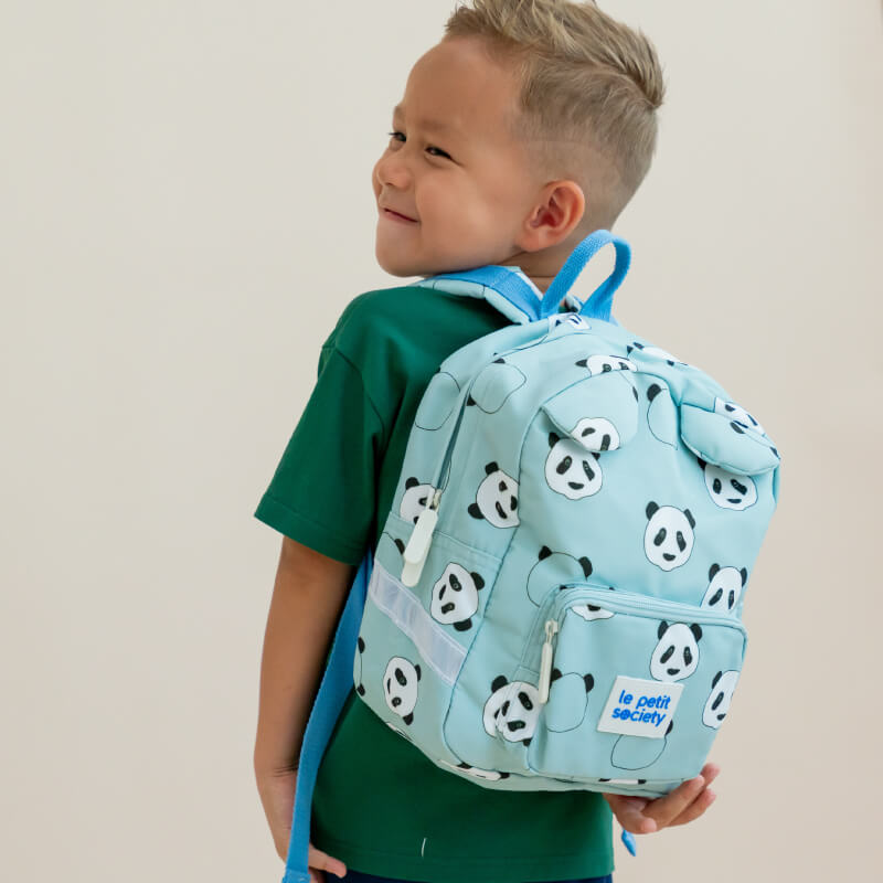 A toddler boy carrying a mint green school bag with a panda print.