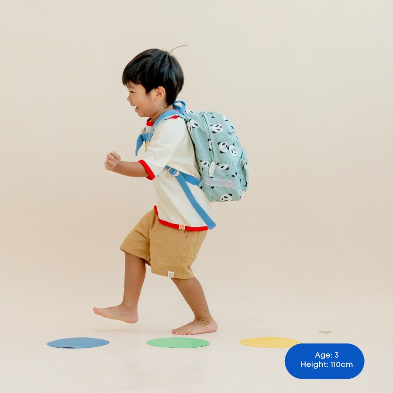 A toddler walking with a mint green, panda-print school bag. 