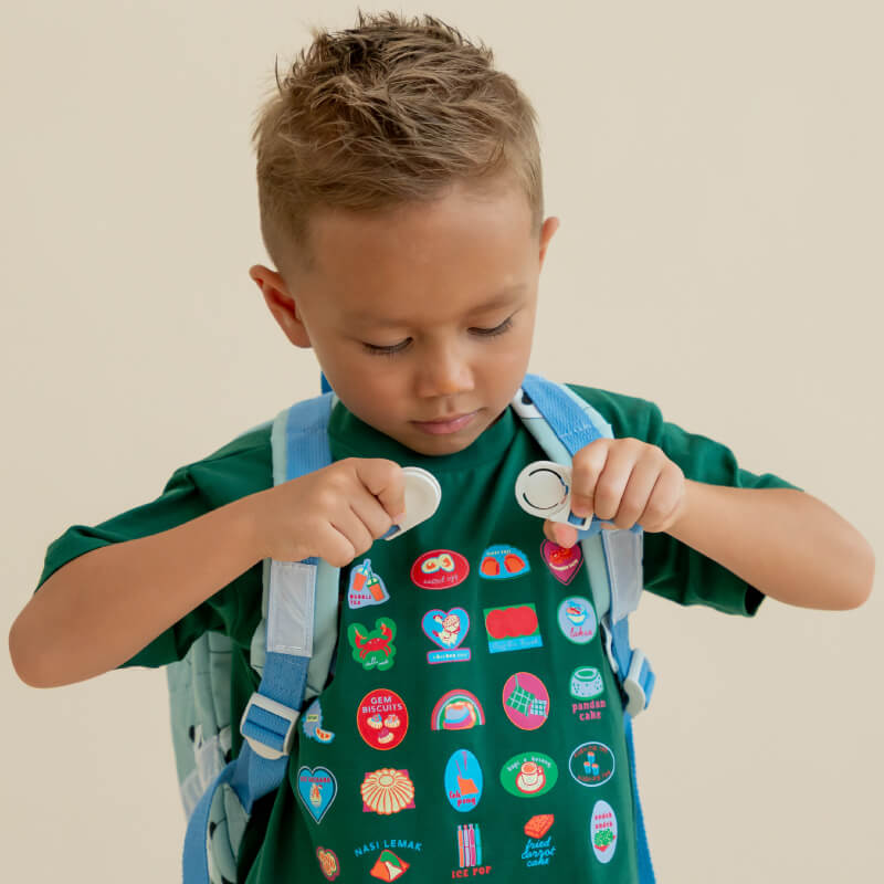 A preschool boy securing the buckle clasp of his school bag.