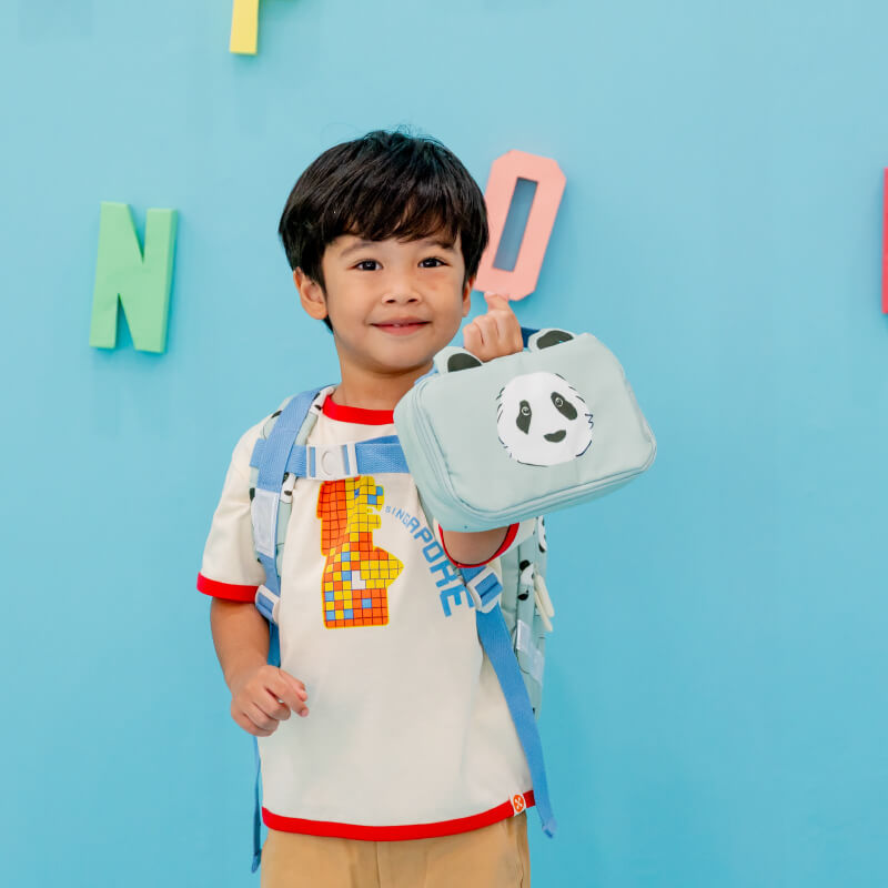 A little boy carrying a mint blue pencil case and pouch with a panda print and ears.