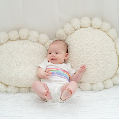 A baby wearing a white romper with a pastel rainbow print from Le Petit Society's rainbow series.