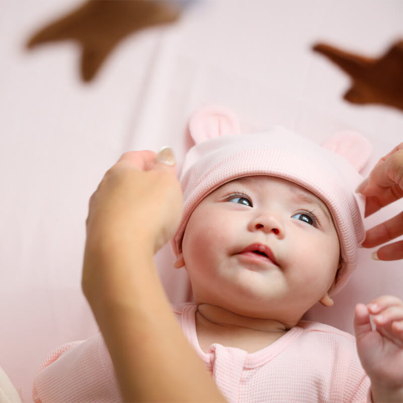 A baby wearing an organic bear hat in pink by Le Petit Society.