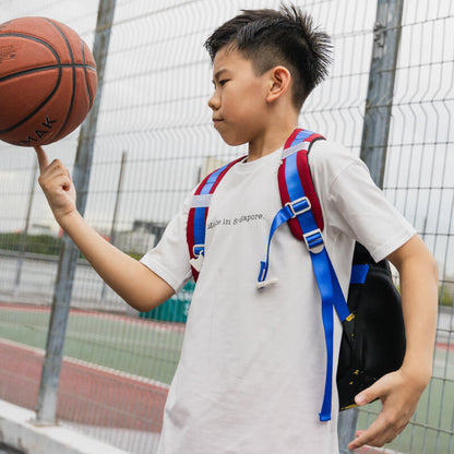A sporty primary school boy playing basketball while carrying the LPS kids single pocket school bag.