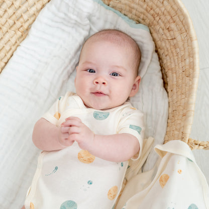 A baby wearing a kimono romper by Le Petit Society, featuring a print of planets over a cream base. 