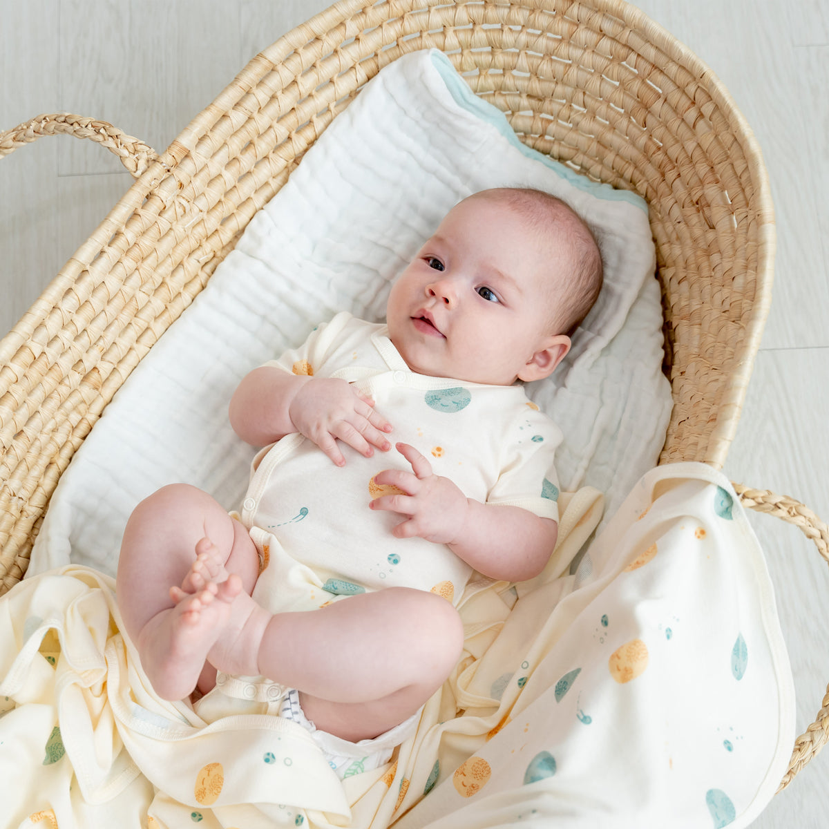 A baby wearing a kimono romper by Le Petit Society, featuring a print of planets over a cream base. 
