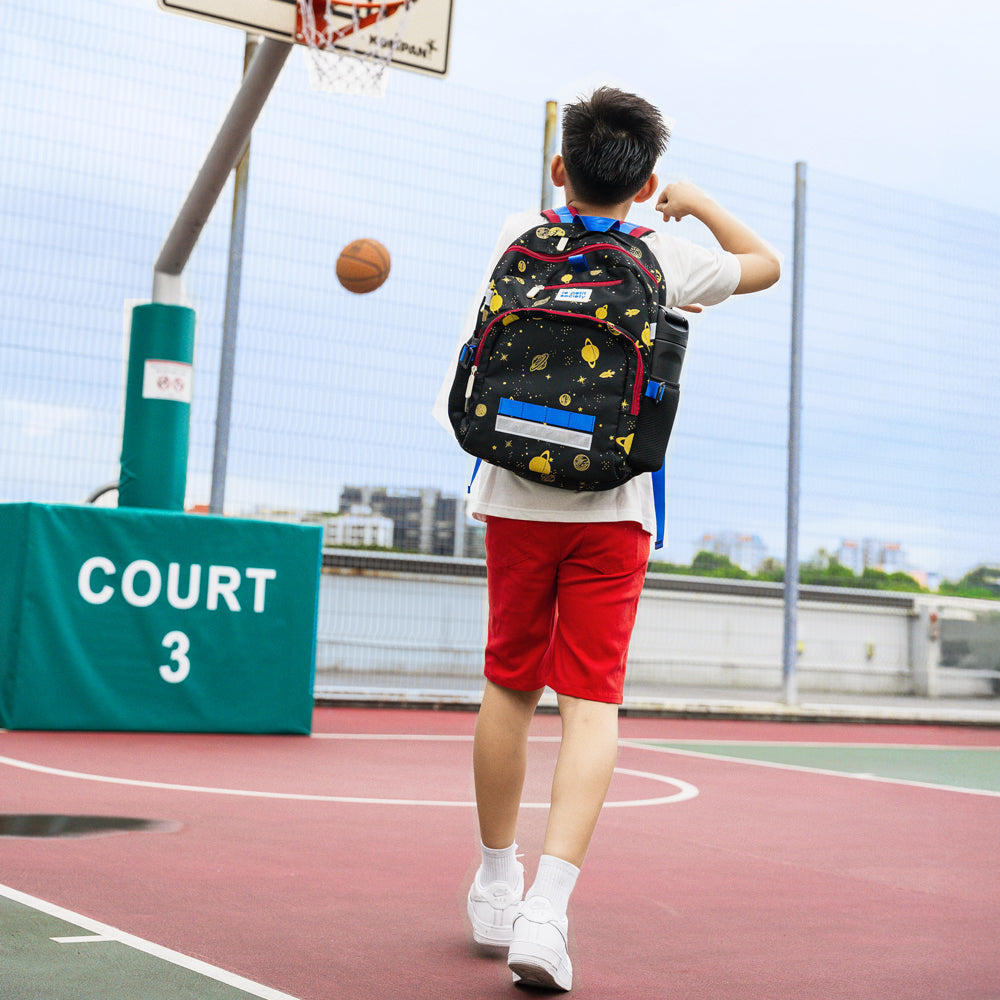 An athletic primary school boy playing basketball with the kids single pocket school bag.