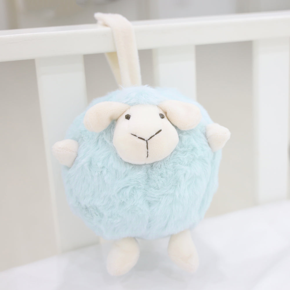 A round and plush sheep toy in soft blue by Le Petit Society hangs off the frame of a baby cot.