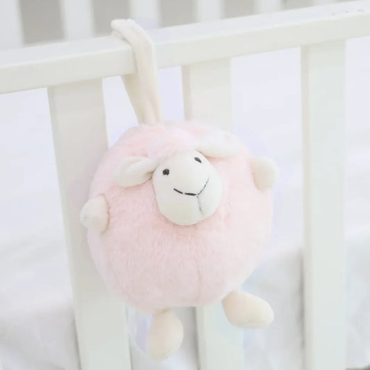 A round and plush sheep toy in soft pink by Le Petit Society hangs off the frame of a baby cot.