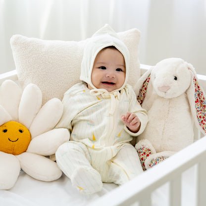 A baby wearing a matching organic bonnet hat and sleepsuit in sail boat print from Le Petit Society.