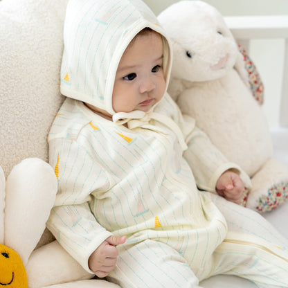 A baby wearing a matching organic bonnet hat and sleepsuit in sail boat print from Le Petit Society.