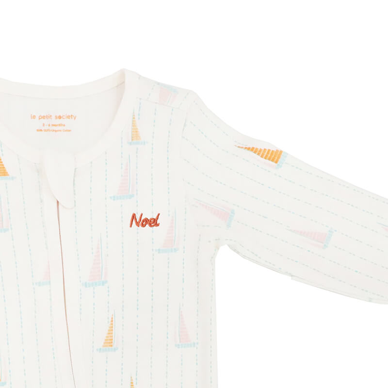 A close-up of a name embroidery personalisation of an organic baby zip sleepsuit in sail boat print from Le Petit Society.