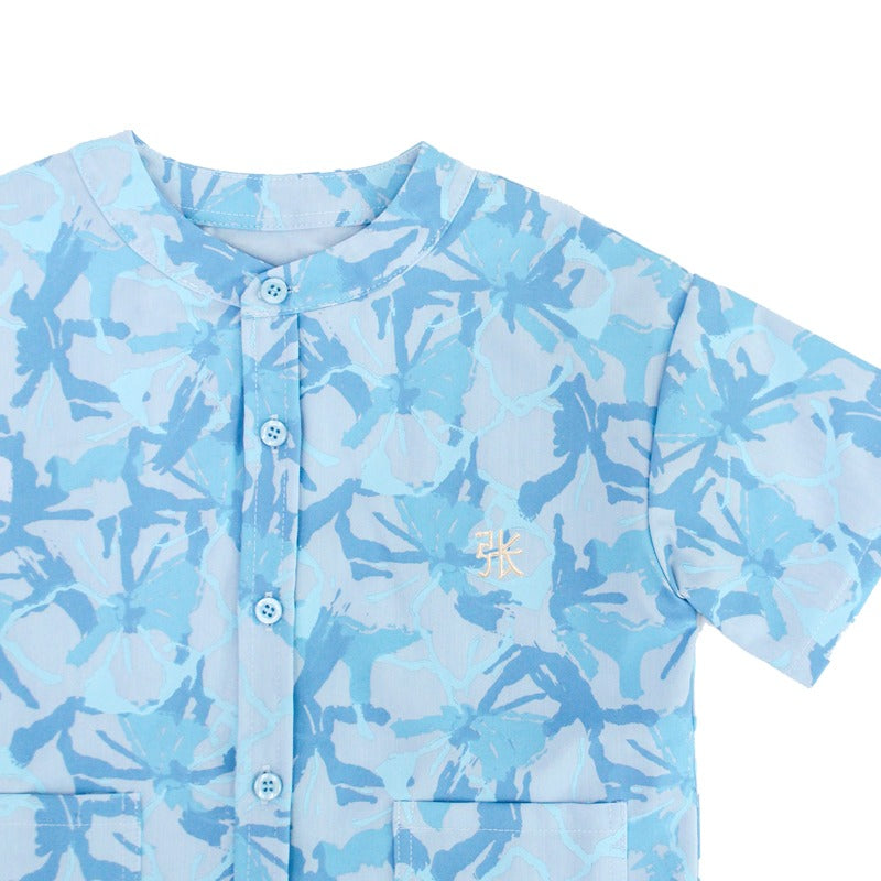 Close-up of a light blue boys’ shirt from the Le Petit Society x Sheila Sim CNY 2026 collection, featuring a tonal floral horse print, blue buttons, and a small yellow embroidered Chinese character on the chest. The shirt has a round neckline and short sl