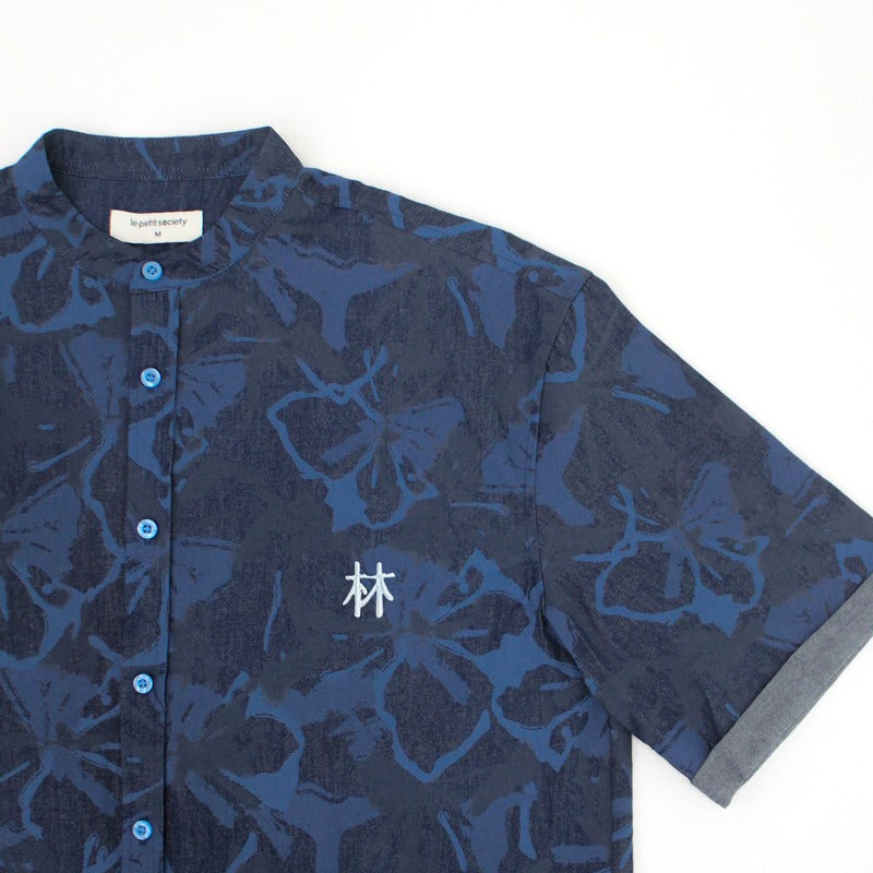 Close-up of a navy blue chambray men’s shirt from the Le Petit Society x Sheila Sim CNY 2026 collection, featuring a tonal floral horse print, blue buttons, and a small white embroidered Chinese character on the chest. The shirt has a stand collar and fol