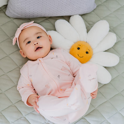 A baby wearing a pink zip sleepsuit and bow headband in a rabbit print by Le Petit Society,