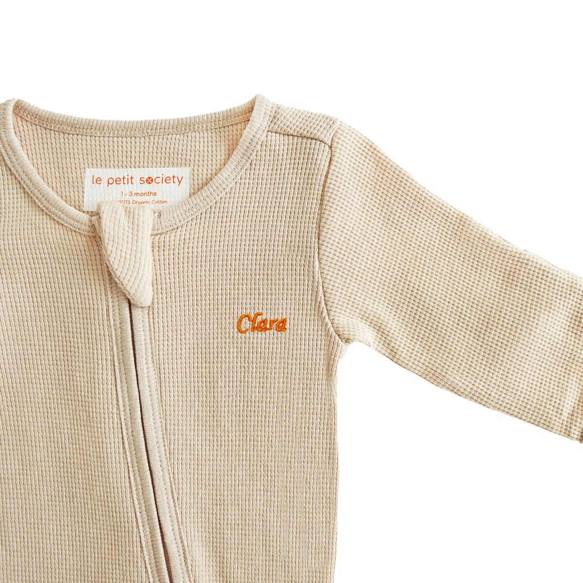 An organic baby zip sleepsuit in beige with a name embroidery personalisation, by Le Petit Society.
