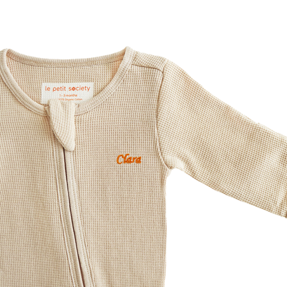 An organic baby zip sleepsuit in beige with a name embroidery personalisation, by Le Petit Society.
