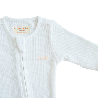 An organic baby zip sleepsuit in white with a name embroidery personalisation, by Le Petit Society.
