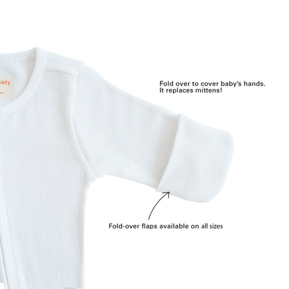 A baby organic zip sleepsuit in white by Le Petit Society, with fold over flaps at the sleeves to cover a baby's hands, acting as a substitute for mittens.
