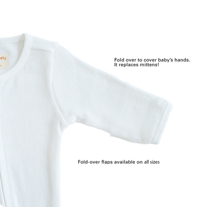 A baby organic zip sleepsuit in white by Le Petit Society, with fold over flaps at the sleeves to cover a baby's hands, acting as a substitute for mittens.
