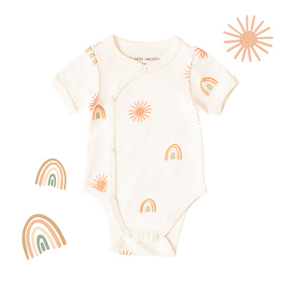 A baby kimono romper by Le Petit Society, featuring a print of sun and rainbows over a cream base. 
