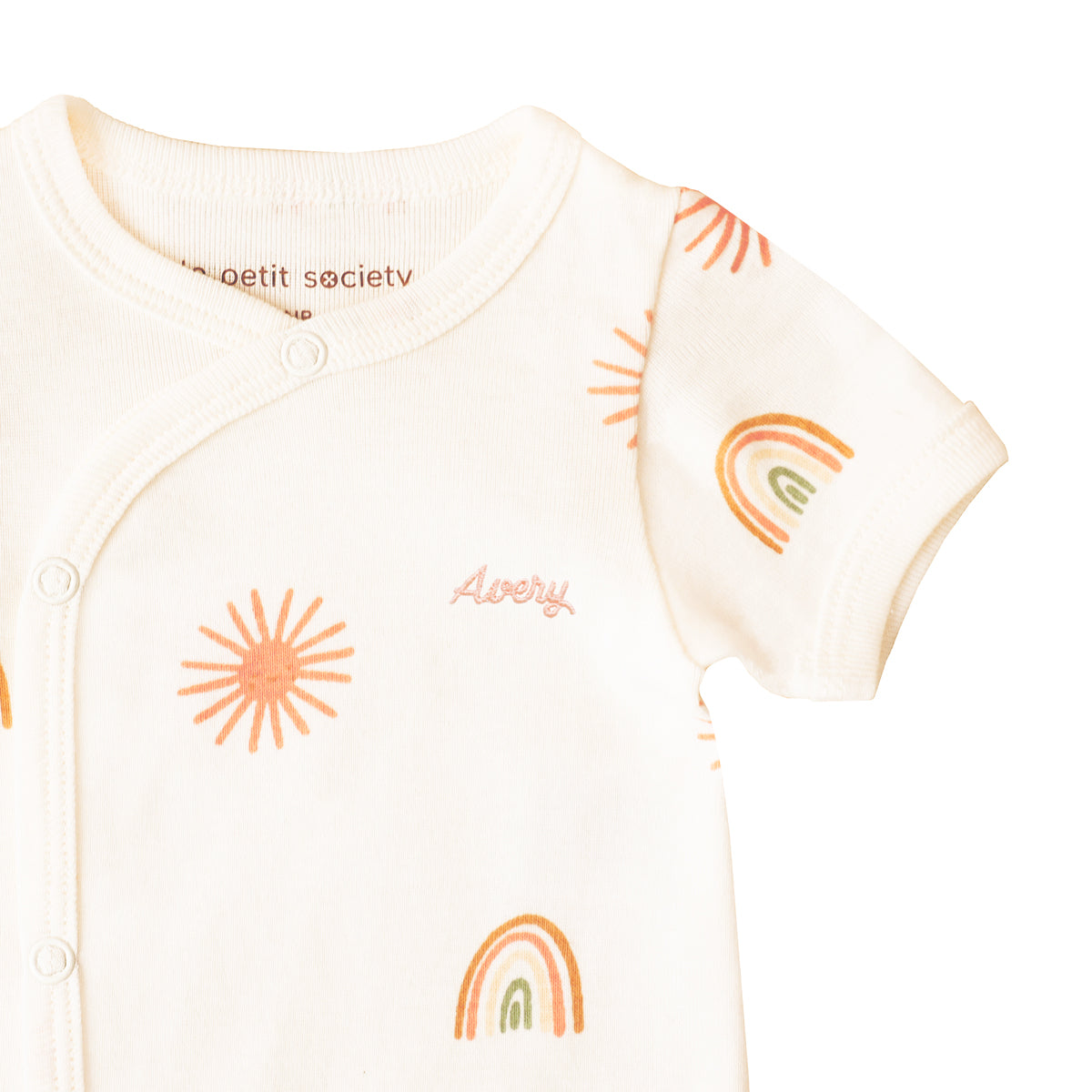 A close-up of a personalised name embroidery on a baby kimono romper featuring a print of sun and rainbows from Le Petit Society.