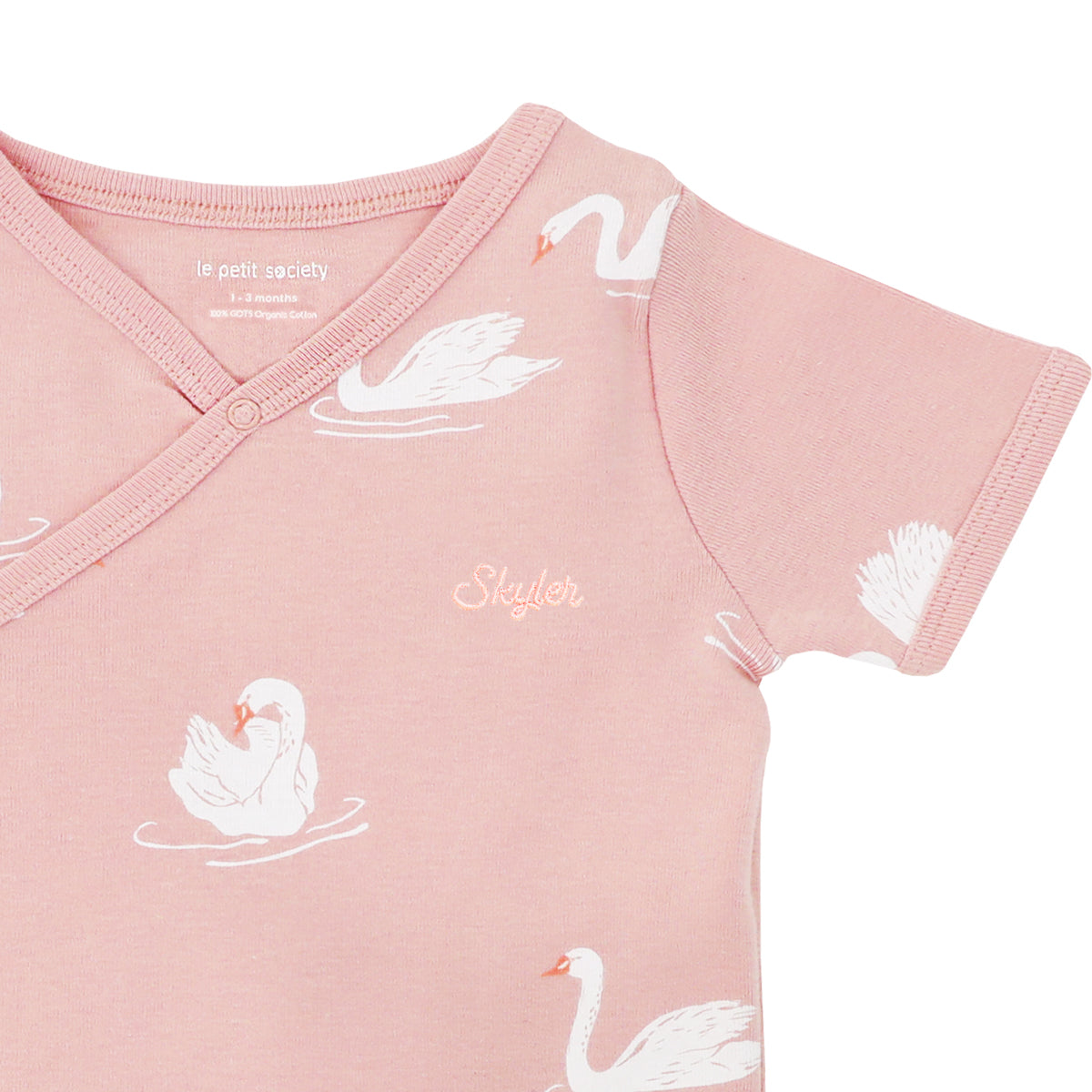 A close-up of a personalised name embroidery on a A peach-coloured baby kimono romper by Le Petit Society, featuring a print of swans.