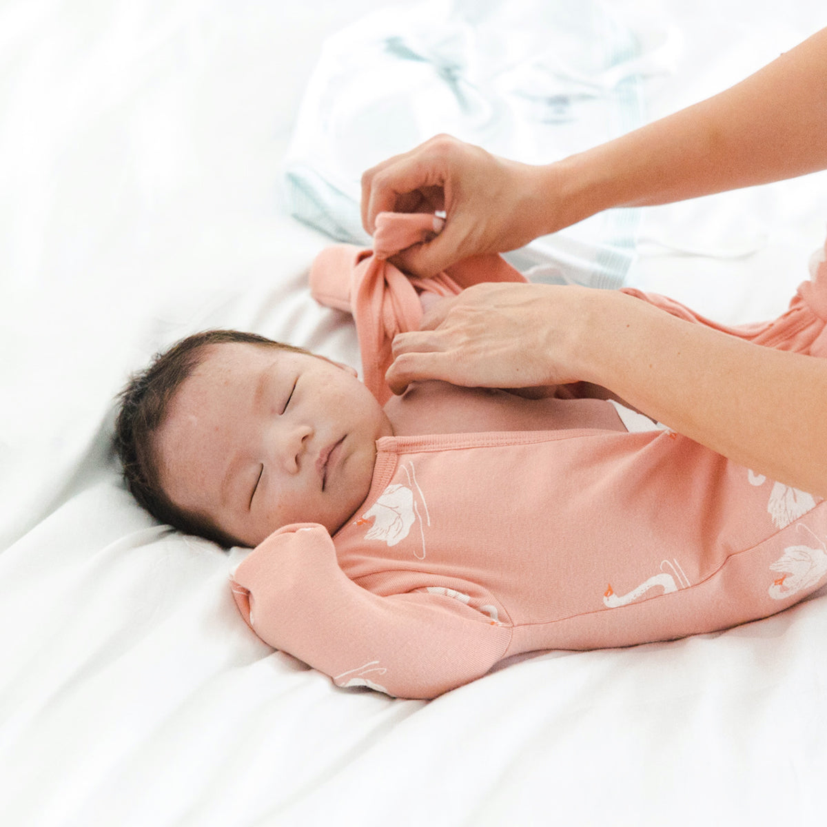 A newborn baby wearing an organic zip sleepsuit in peach with foldable mittens and footies by Le Petit Society, featuring a print of swans.