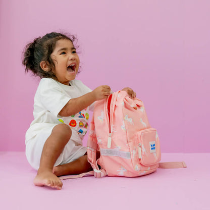 Toddler smiling with a pink unicorn print preschool bag.