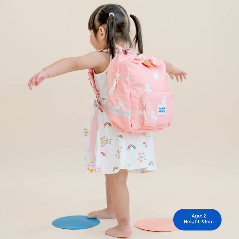 Little girl carrying a pink unicorn print preschool bag.