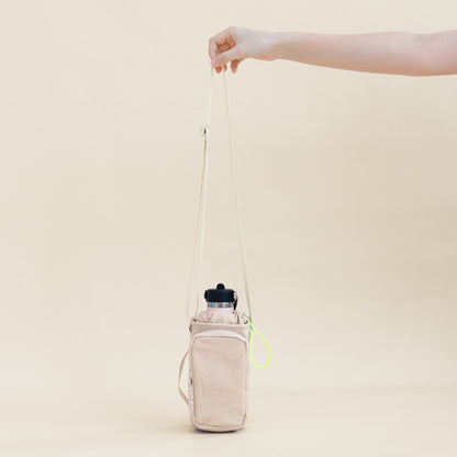 A hand holding on to the adjustable strap of a water bottle sling bag.