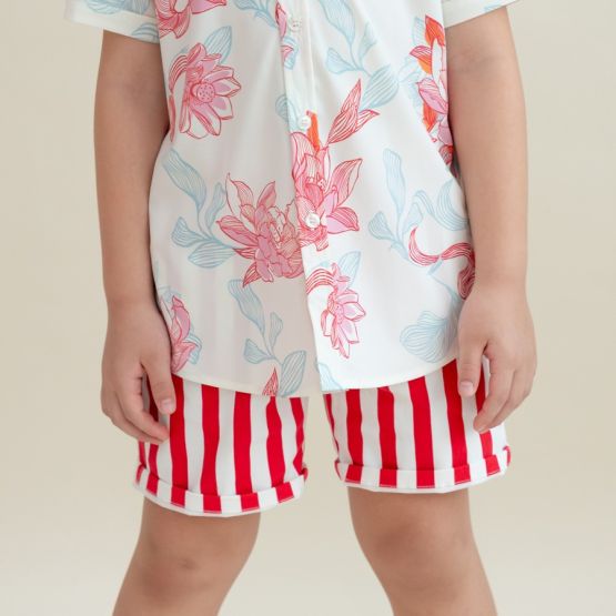A child wearing red and white vertical striped shorts paired with a white shirt featuring pink and blue floral prints from the Le Petit Society x Sheila Sim CNY 2026 collection. The close-up shows the shorts’ rolled cuffs and the vibrant floral pattern on