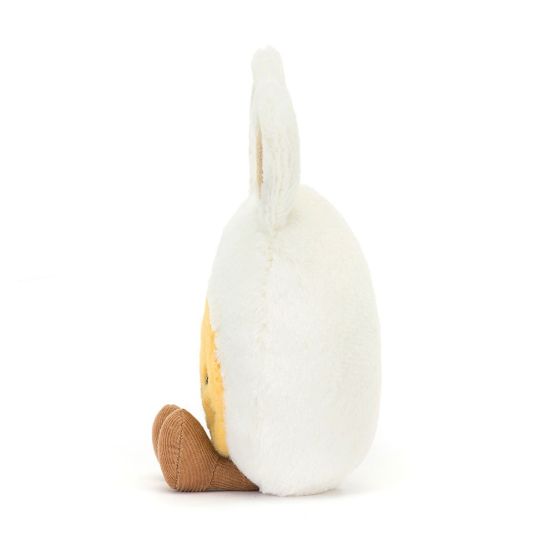 A side view of a egg shaped soft plush toy with bunny ears and a yellow face with whiskers. It has black button eyes, a pink embroidered nose, a happy smile, and brown corduroy feet