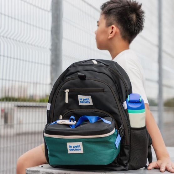 A primary school boy with his double pocket school bag in black and green.