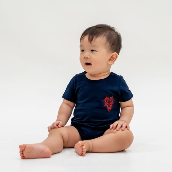 A baby boy in a navy blue romper with a red dragon print from Le Petit Society's Dragon Streetwear collection.