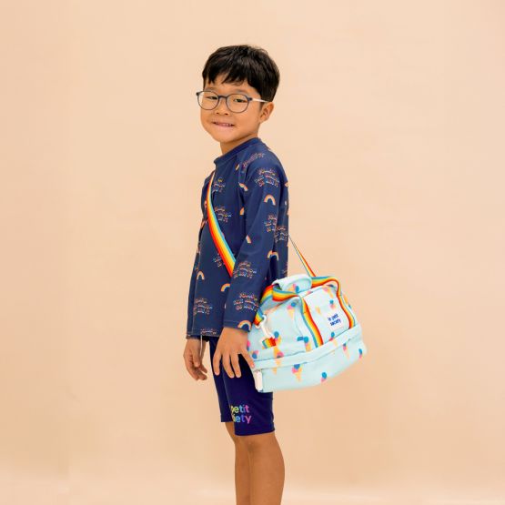 A primary school boy carrying a blue thermal lunch bag with an ice-cream print and rainbow straps.