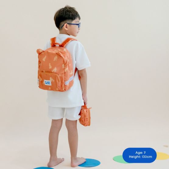 A primary school boy carrying an orange, leopard-print school bag and pencil case.