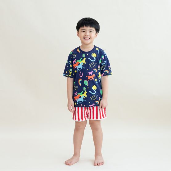 A young boy stands smiling in the Rainbow Horse tee paired with bold red-and-white striped shorts. The vibrant illustrations of horses, stars and rainbows pop against the navy base, giving the outfit a festive, playful look perfect for Lunar New Year.
