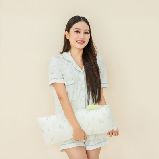 A family of three — mother, father, and baby boy — all wearing matching sleepwear and with pillows featuring a green pear print from Le Petit Society.