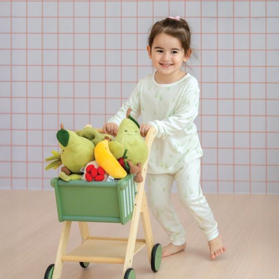 A little girl in a pyjamas set from Le Petit Society, featuring a soft bamboo fabric and a print of green pears.