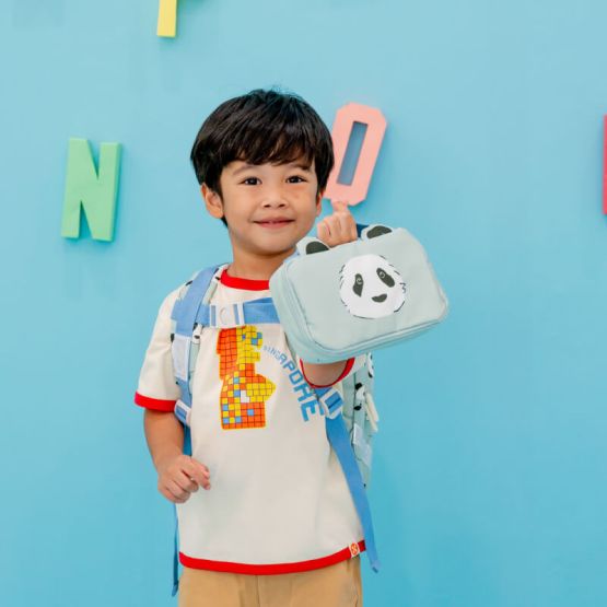A little boy carrying a mint blue pencil case and pouch with a panda print and ears.