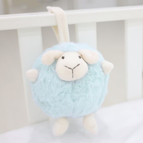 A round and plush sheep toy in soft blue by Le Petit Society hangs off the frame of a baby cot.