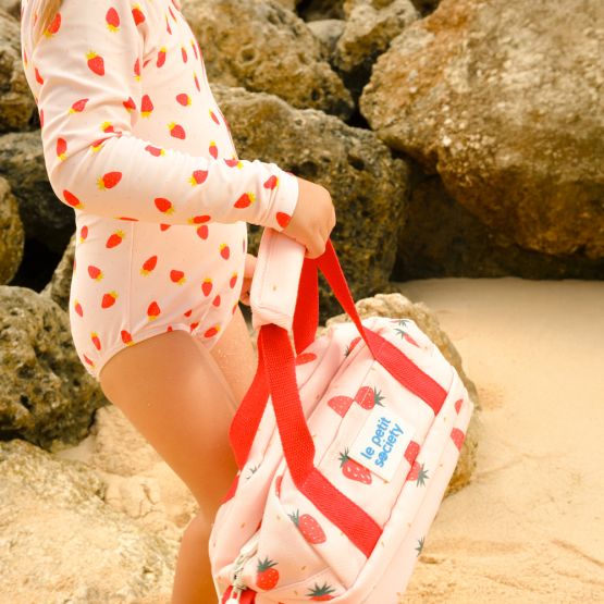 A little girl with a pink strawberry-printed swimsuit and thermal lunch bag from Le Petit Society.
